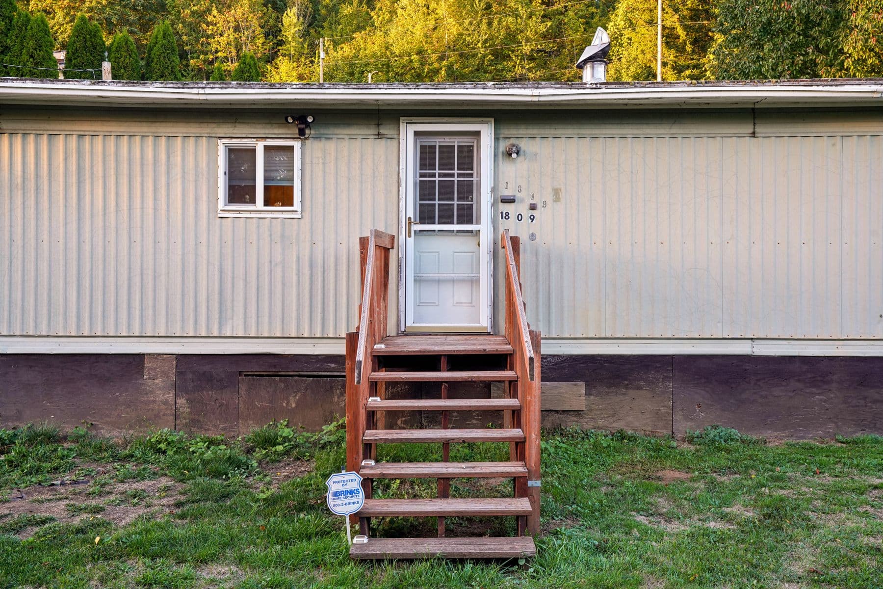 The front of a single-wide mobile home with wooden entry steps, a white door and a grassy yard.