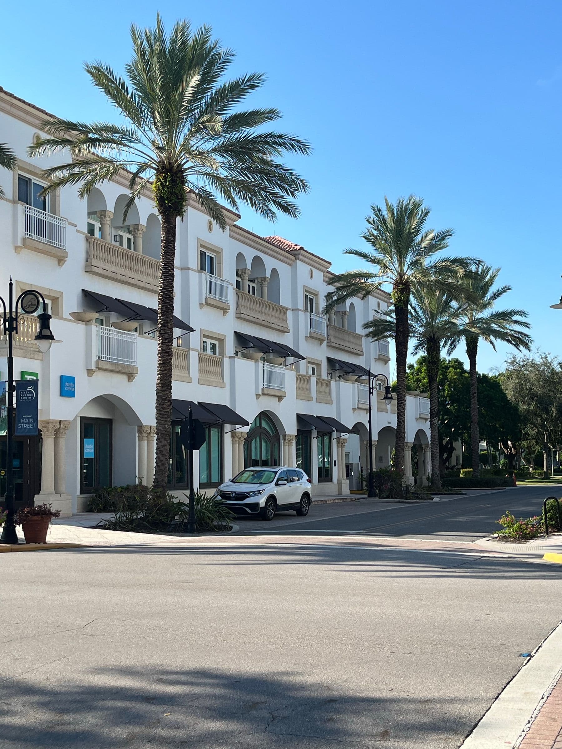 A three-story white building with arched balconies and tall palm trees along a street in Naples, Florida.