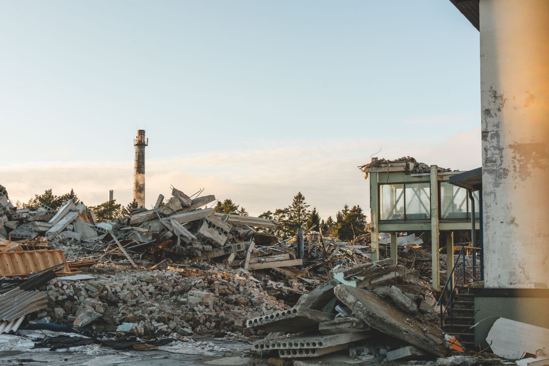 A wide field of broken concrete slabs, bricks and timber with a tall chimney in the distance.
