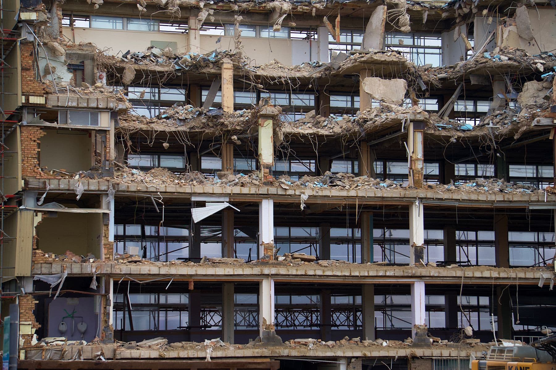 A multistory building with its outer walls gone, leaving exposed floor slabs, columns and hanging rebar.